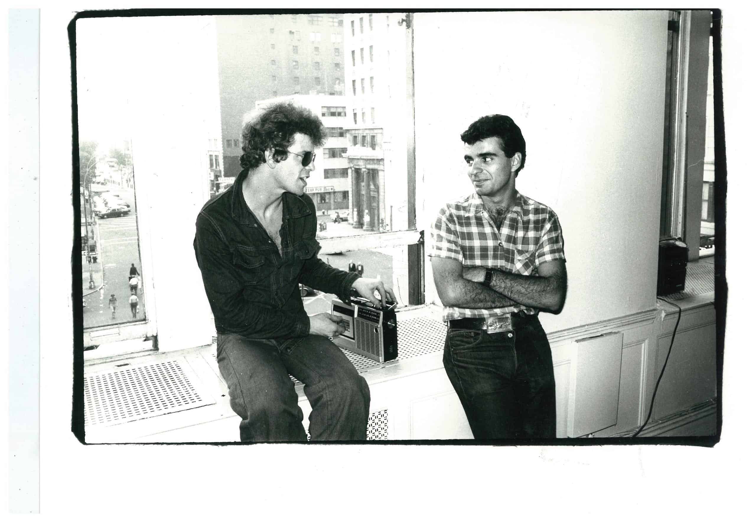 Vintage black-and-white photo of Ronnie Cutrone and Lou Reed seated by a window.