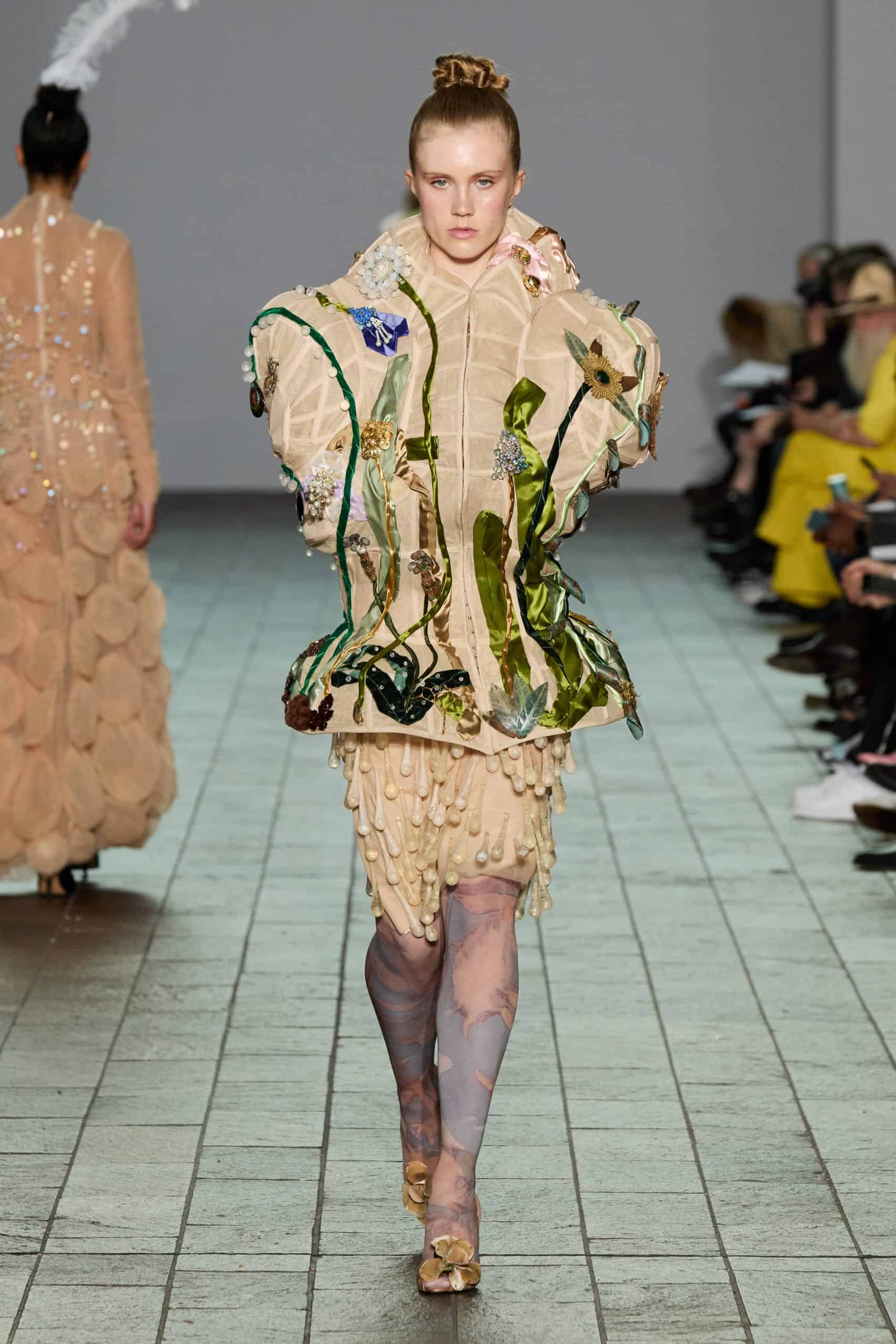 Model wearing an intricate sculptural dress by young designer Anton Femia on the runway, featuring organic textures and green accents. Courtesy of the designer, Anton Femia.