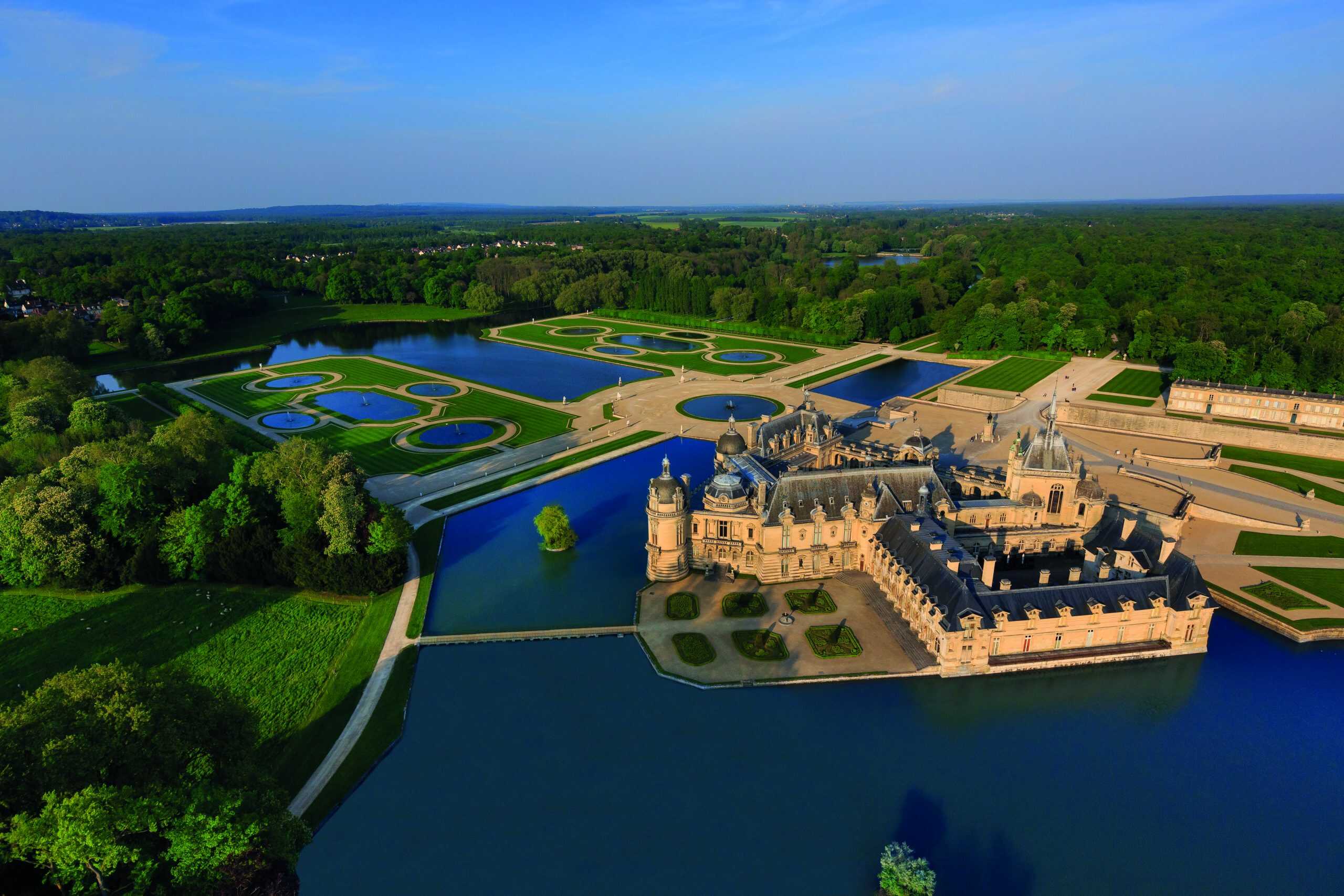 Bird’s-eye view of Château de Chantilly, featuring symmetrical gardens, reflective water features, and lush woodland. Courtesy of Domaine de Chantilly.