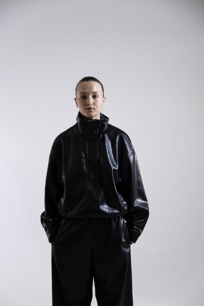 Fashion model in black leather jacket and pants, minimalist style, studio shot.