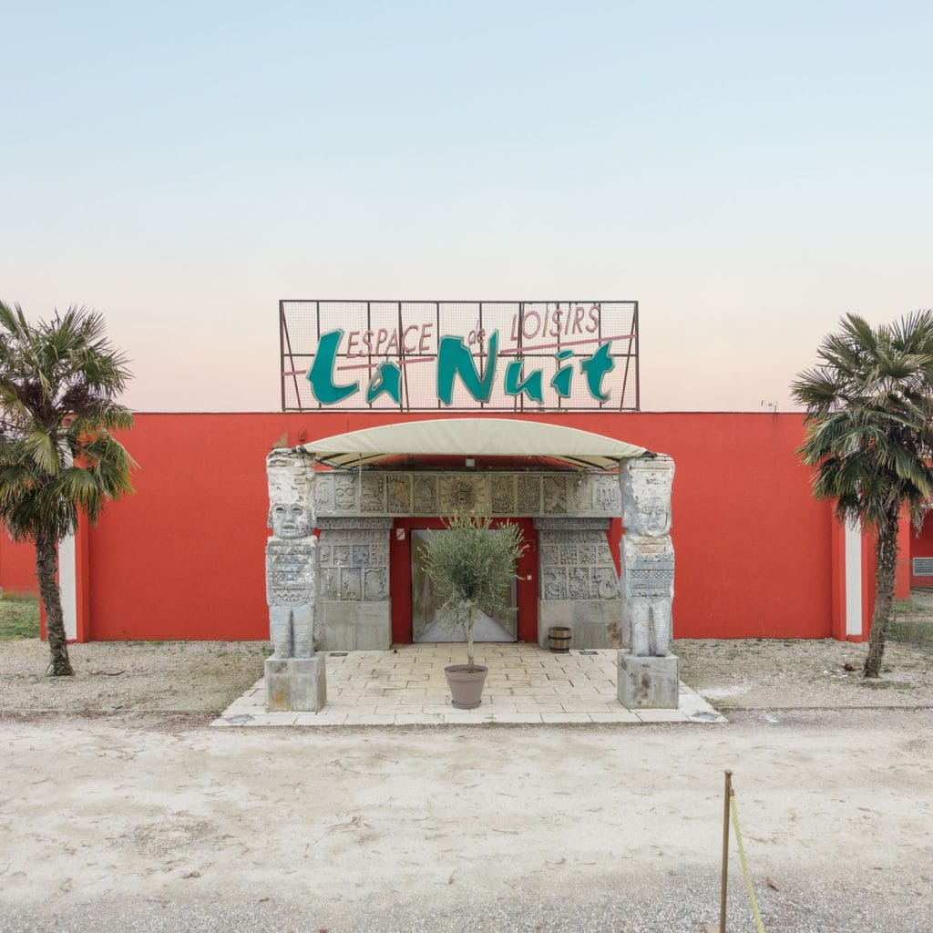 Facade of Espace La Nuit nightclub with classical columns and red walls, under a pale sky.