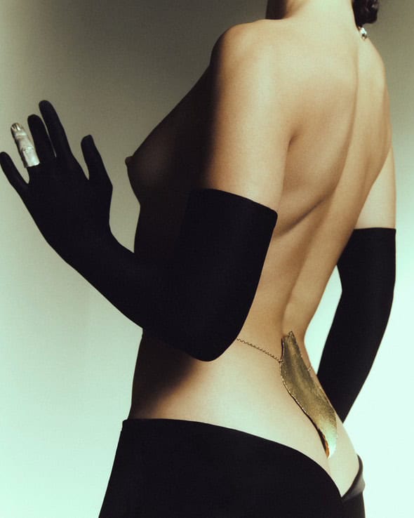 Woman’s back adorned with a gold spine jewel by Incarnem, wearing long black gloves.