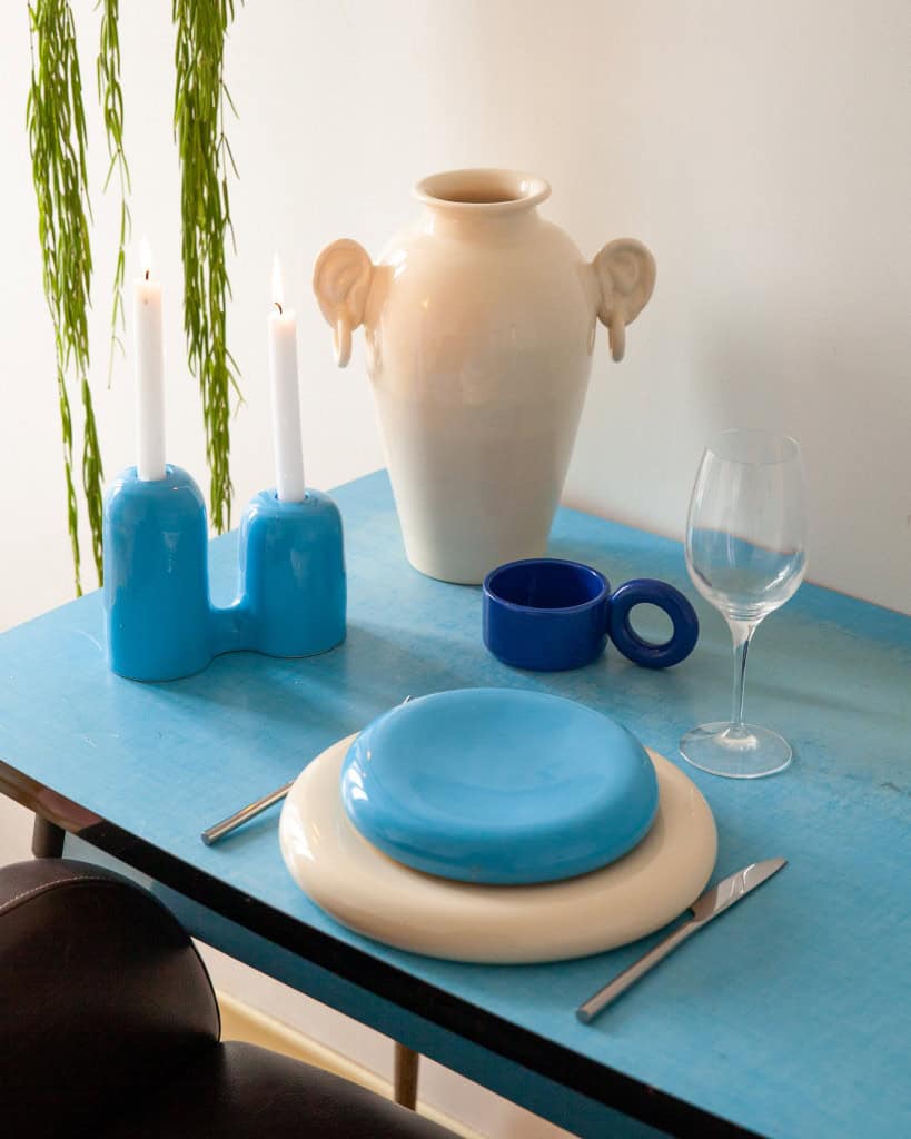 Ceramic ear-handled vase and sculptural candle holder in a playful table setting with stacked round plates by Lola Mayeras.
