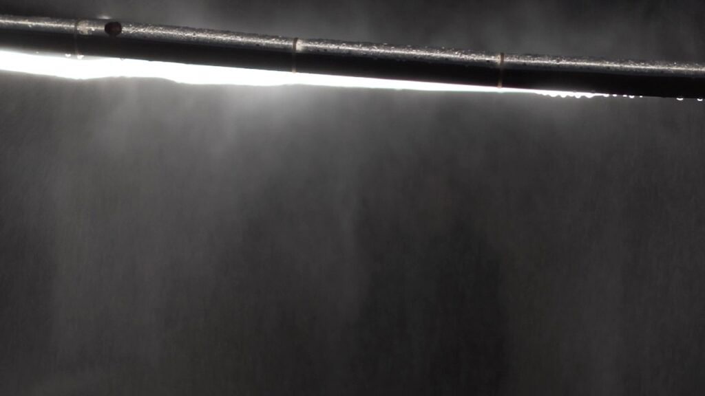 Installation view of Juju Bento's artwork "Rundemanen" from 2022. Tiny drops of water fall off of an illuminated steel circle, suspended in air.