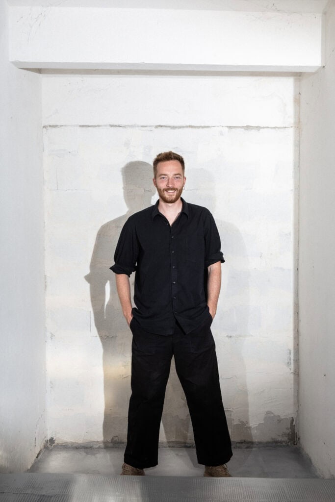 Johan Pertl standing with his cast glass art piece in a minimalist setting.