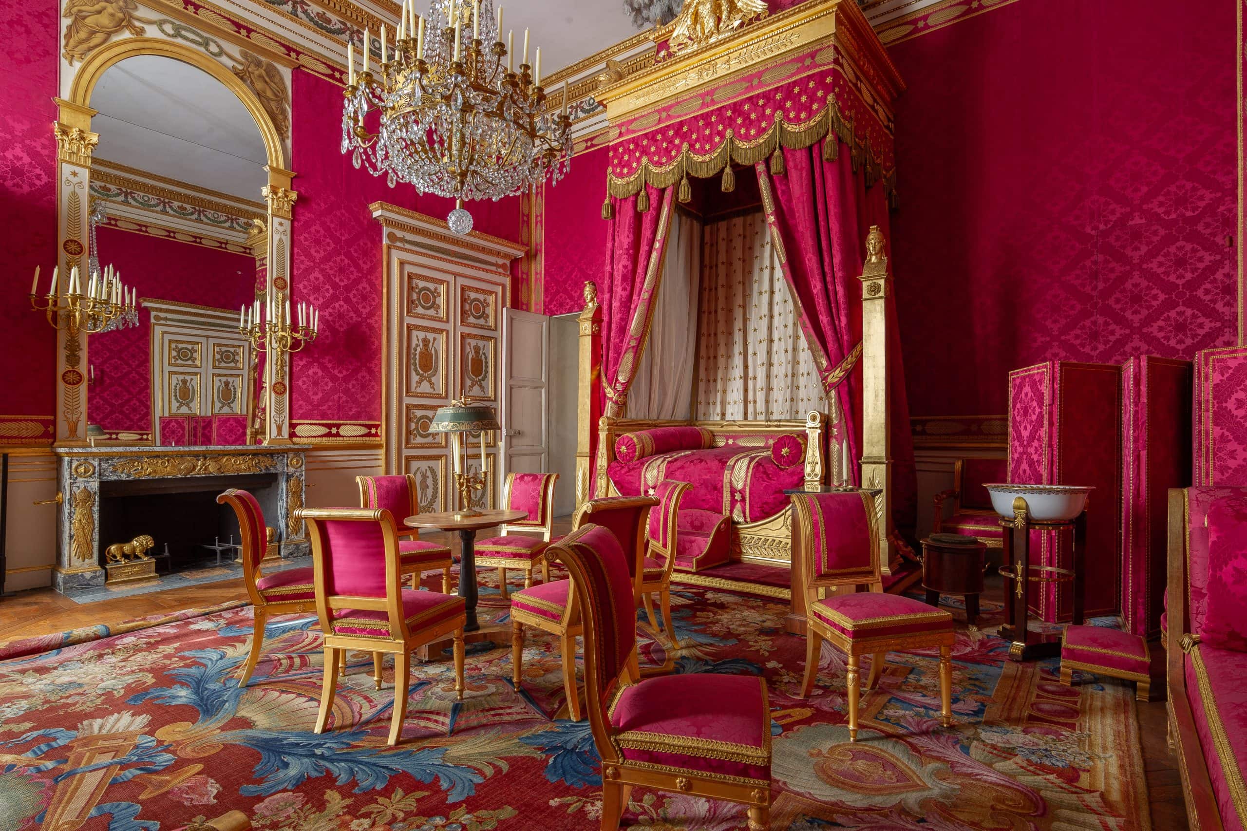 Emperor’s room in Château de Compiègne, featuring crimson walls, gilded moldings, chandeliers, and imperial furniture. Courtesy of Centre des monuments nationaux.