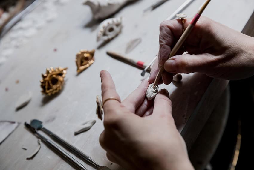 Close-up of hands shaping a porcelain jewel with a sculpting tool.