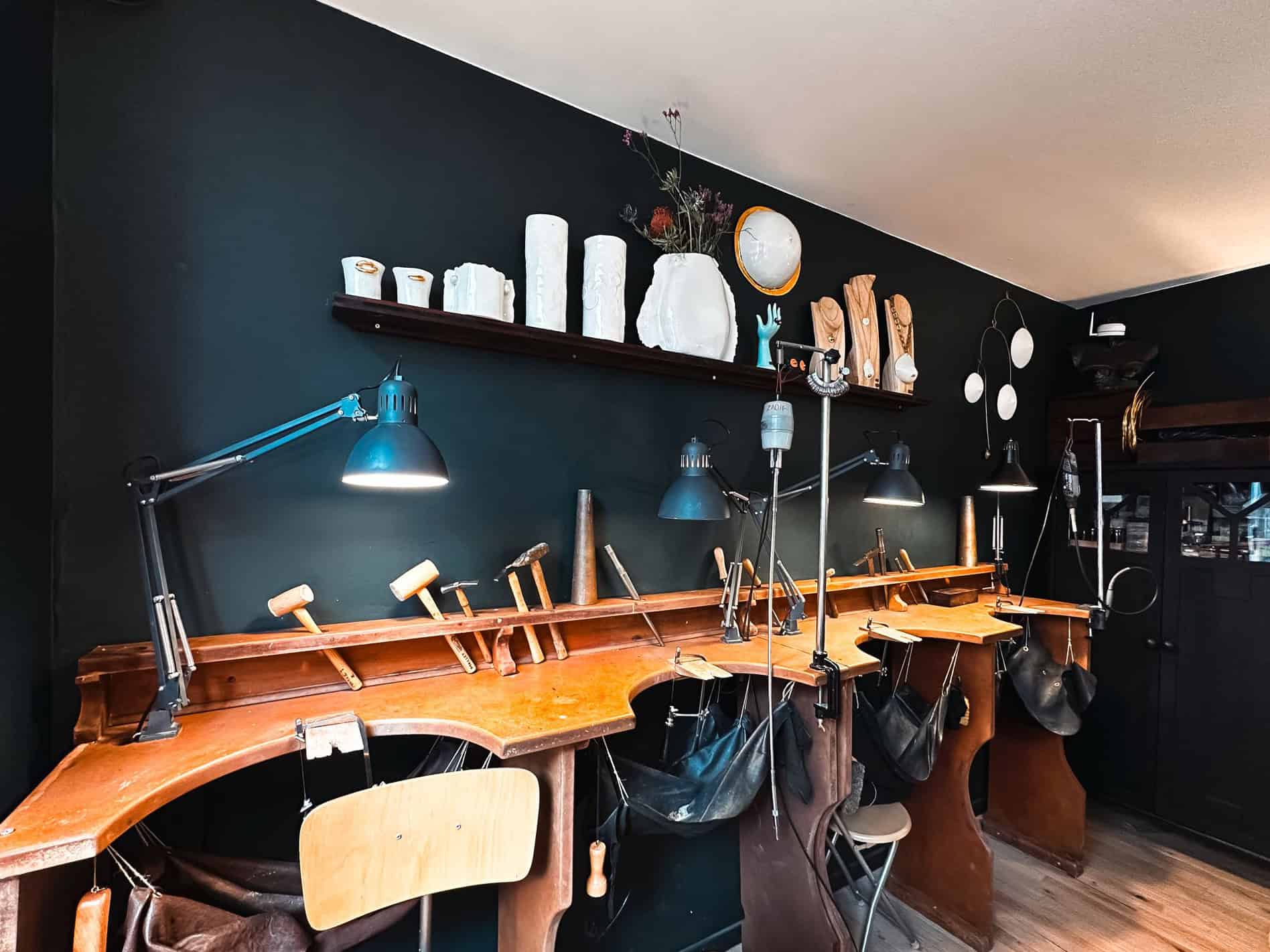 Jordane Somville’s workshop with wooden benches, ceramic molds, and sculpting tools under a black wall.