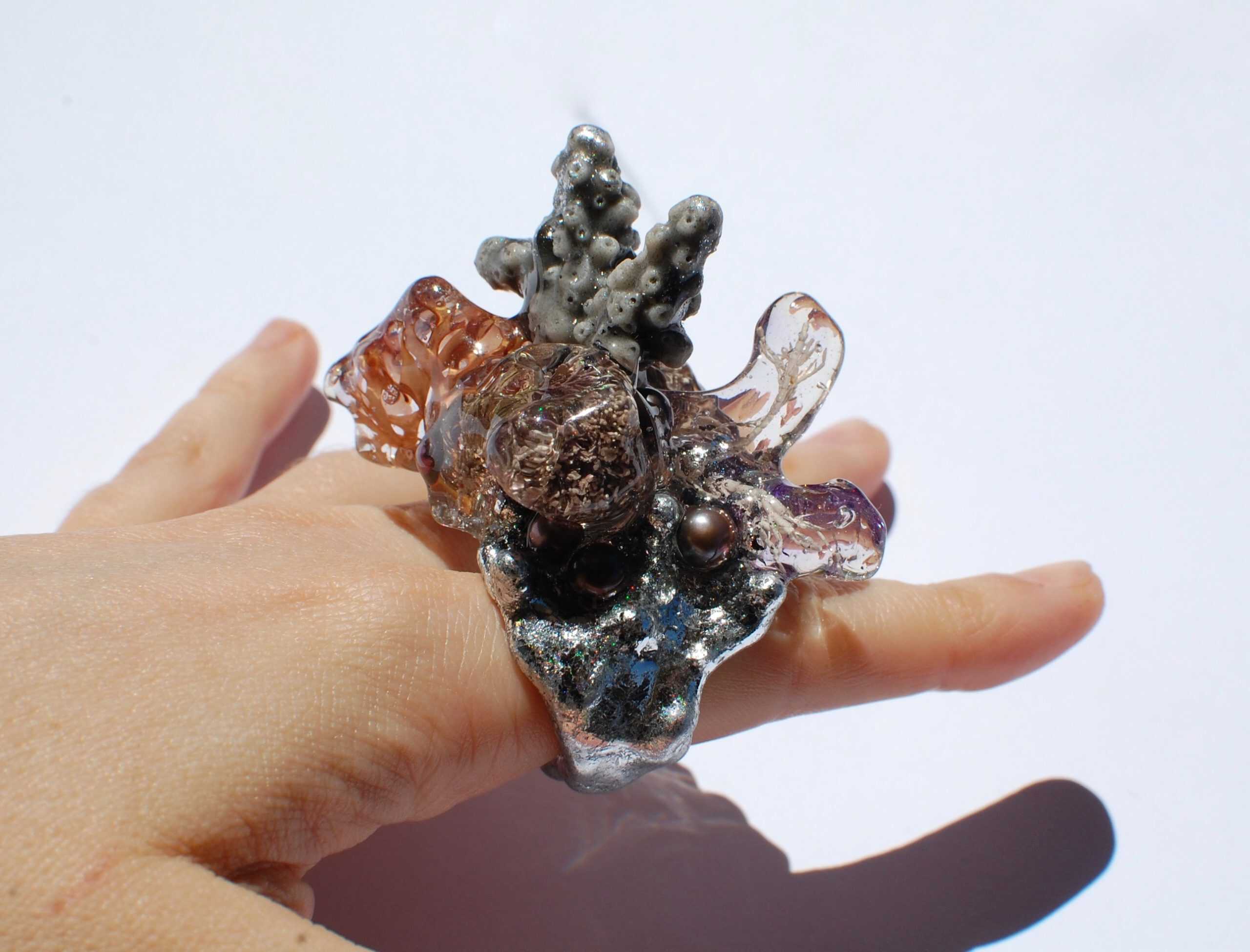 Hand wearing a large, organic-shaped ring featuring glass and pearl details. jam inc jewelry 