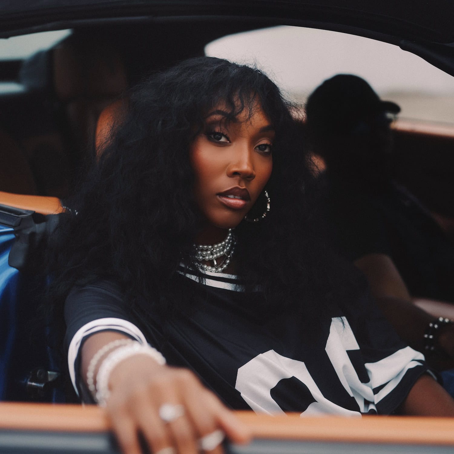 R&B artist Danni Baylor posing in a car, wearing layered pearl jewelry and a black jersey, ahead of her debut EP release. DANNI BAYLORS