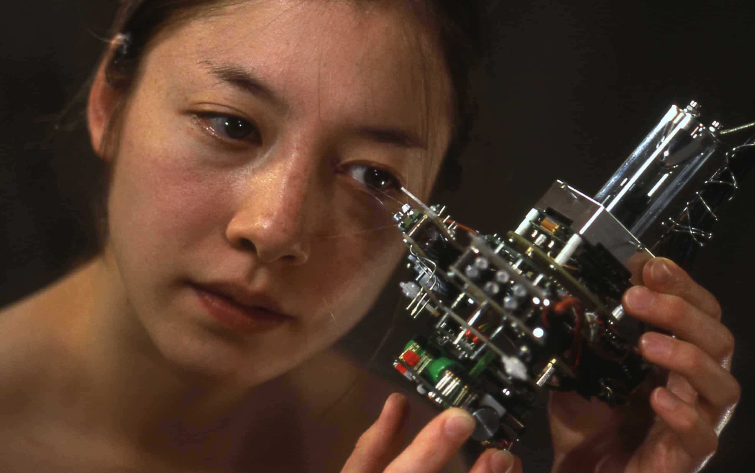 Young woman examining a complex robotic art piece at IRK Magazine exhibition.