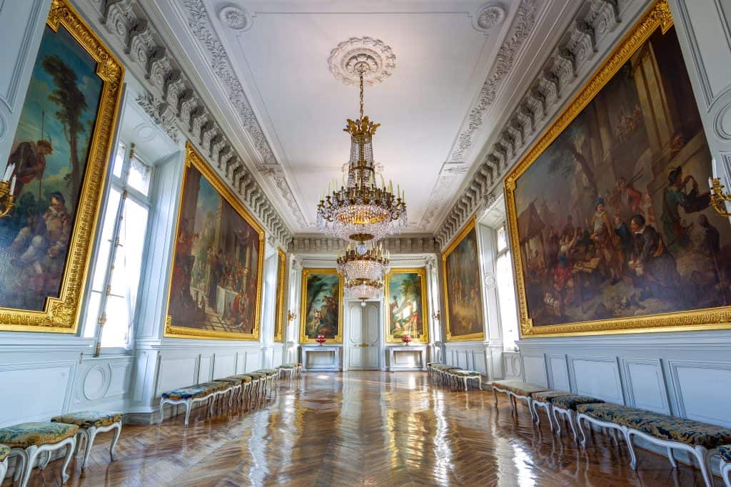 Galerie Natoire in Château de Compiègne, a long hall with parquet floors, chandeliers, and classical paintings. Courtesy of Centre des monuments nationaux.