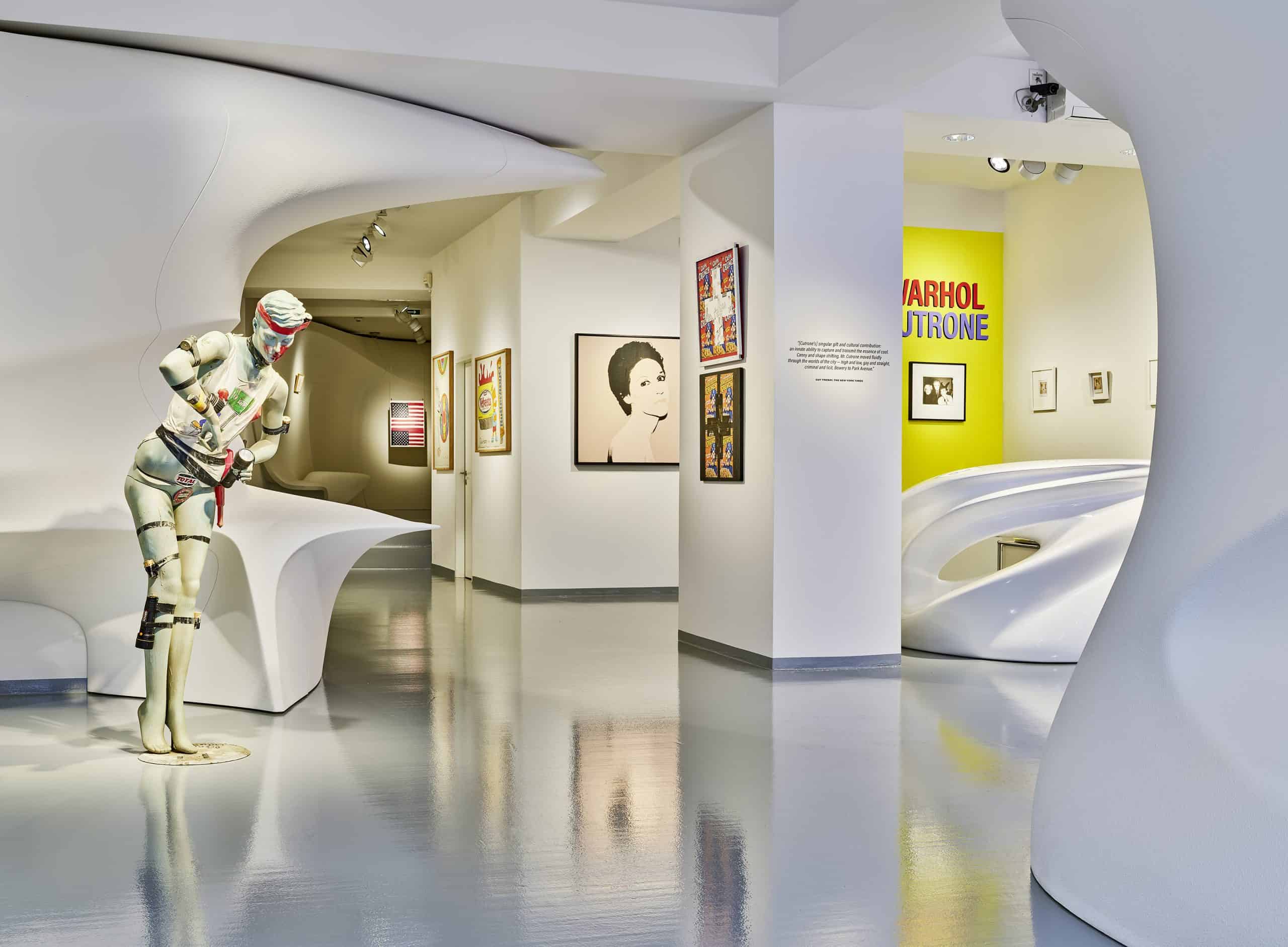 View of Warhol/Cutrone exhibition at Galerie Gmurzynska, with sculpture and framed works in a curved white room.