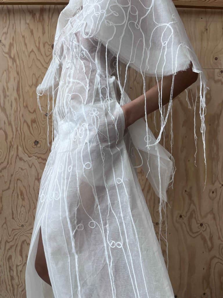 Close-up of a white embroidered dress by Hannah Smith, with cascading threads and anatomical embroidery.