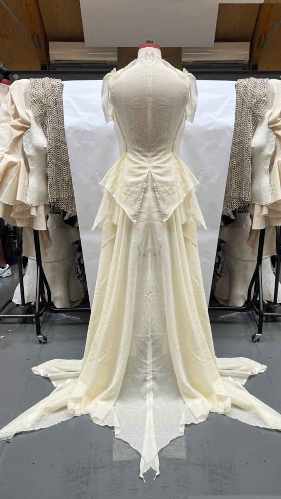  Back view of a long cream gown, showing a bustle-inspired train and corset-like structure.