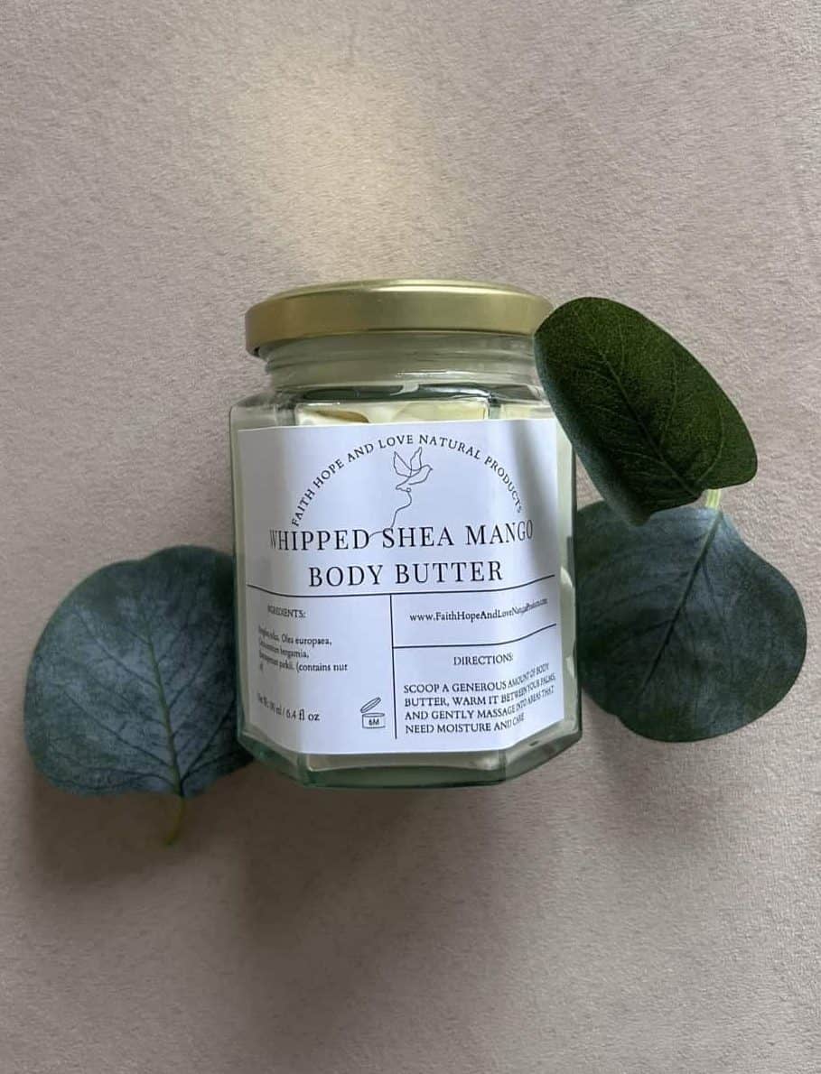 Glass jar of FHL Natural Products’ Whipped Shea Mango Body Butter, styled with green leaves on a beige background. Courtesy of FHL Natural Products.