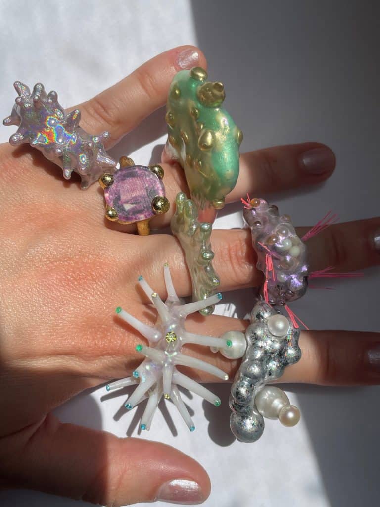 Fingers covered in multiple sculptural, colorful rings.