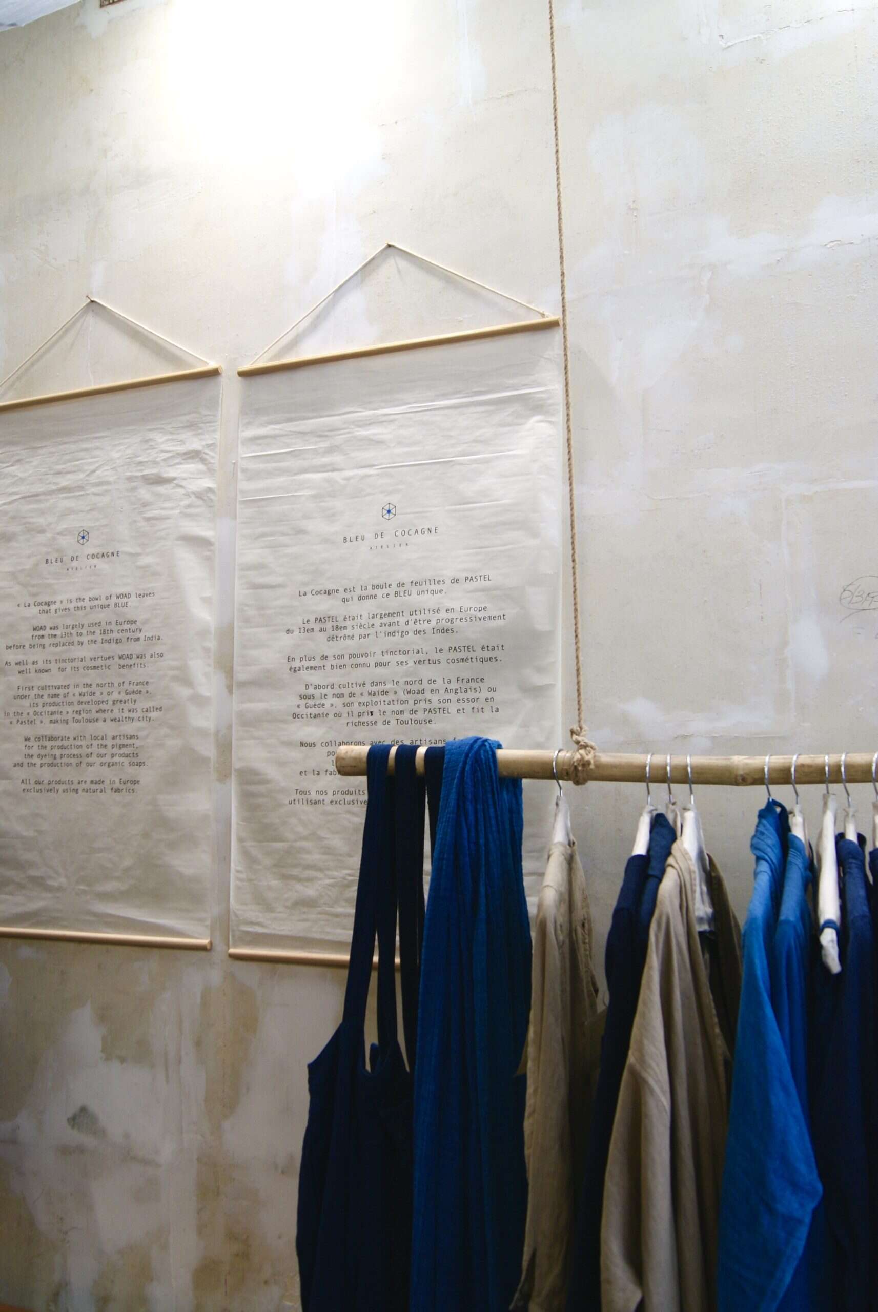 Garments and hand-written textile hangings at Bleu de Cocagne Paris showroom, showcasing woad blue.