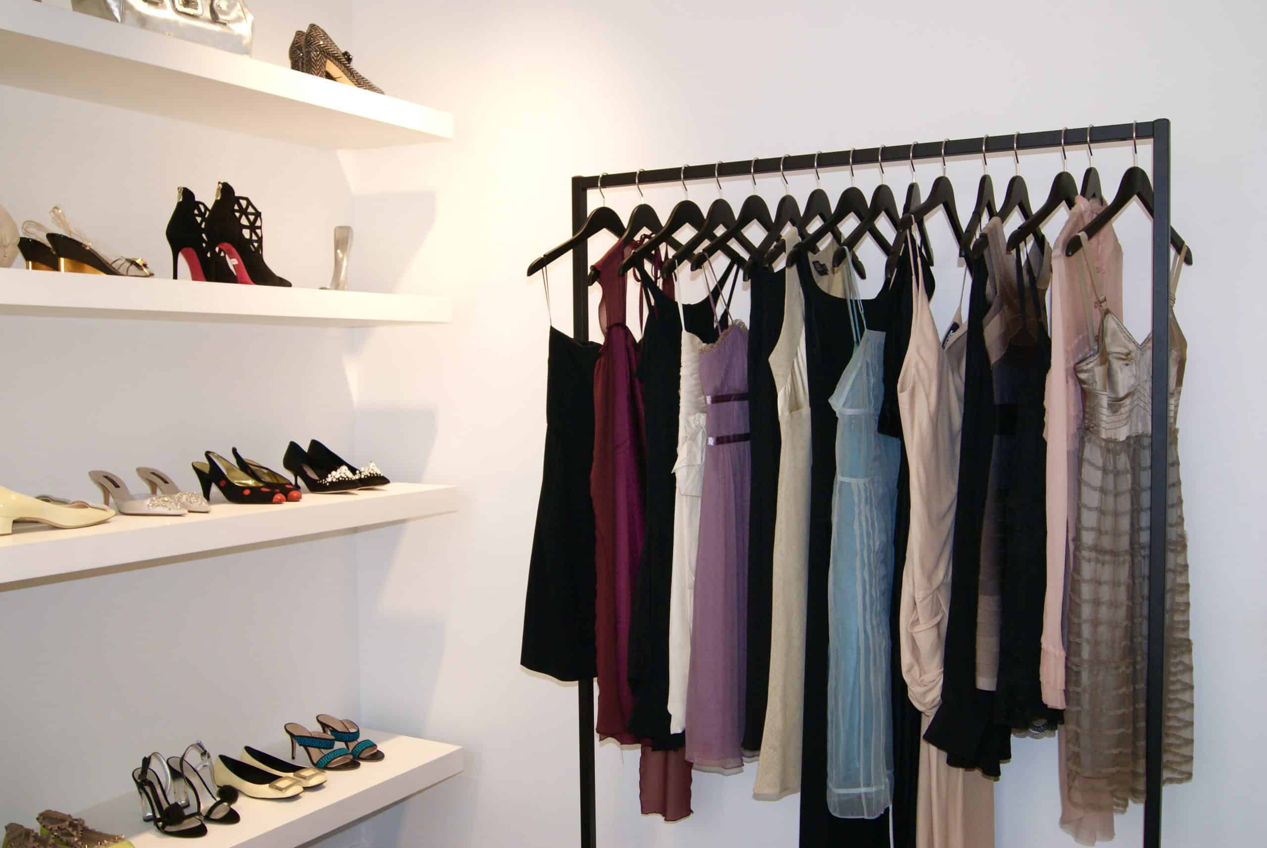Vintage evening dresses on a rack with designer heels displayed on white shelves at Tallon Vintage boutique in Paris