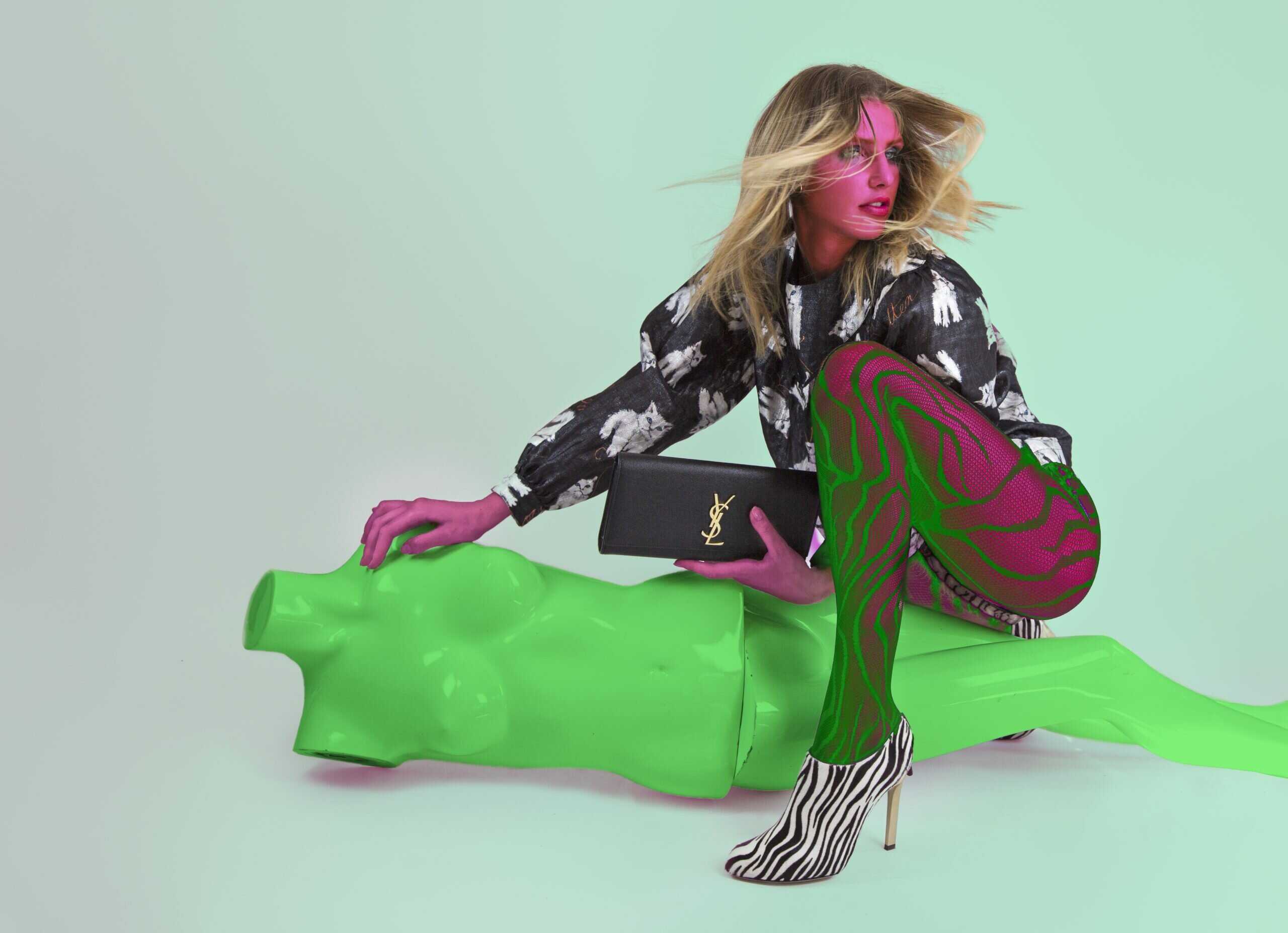 avant-garde styling, sitting on green prop with patterned tights and bold jacket, high-fashion editorial shot.