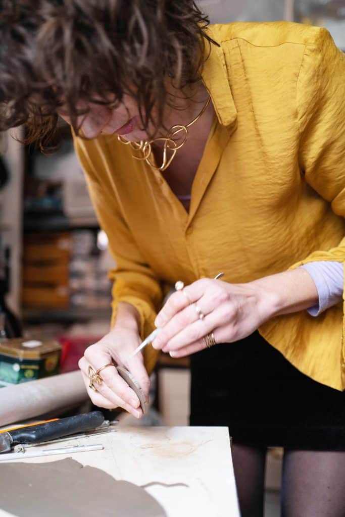 Jordane Somville shaping a piece at her desk, wearing a mustard-colored top.