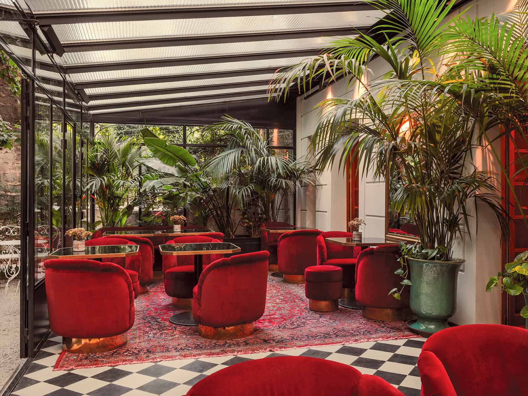 Hotel Particulier, a garden hideawayl ounge area at Hôtel Particulier Montmartre featuring red velvet chairs, tropical plants, and a glass roof.