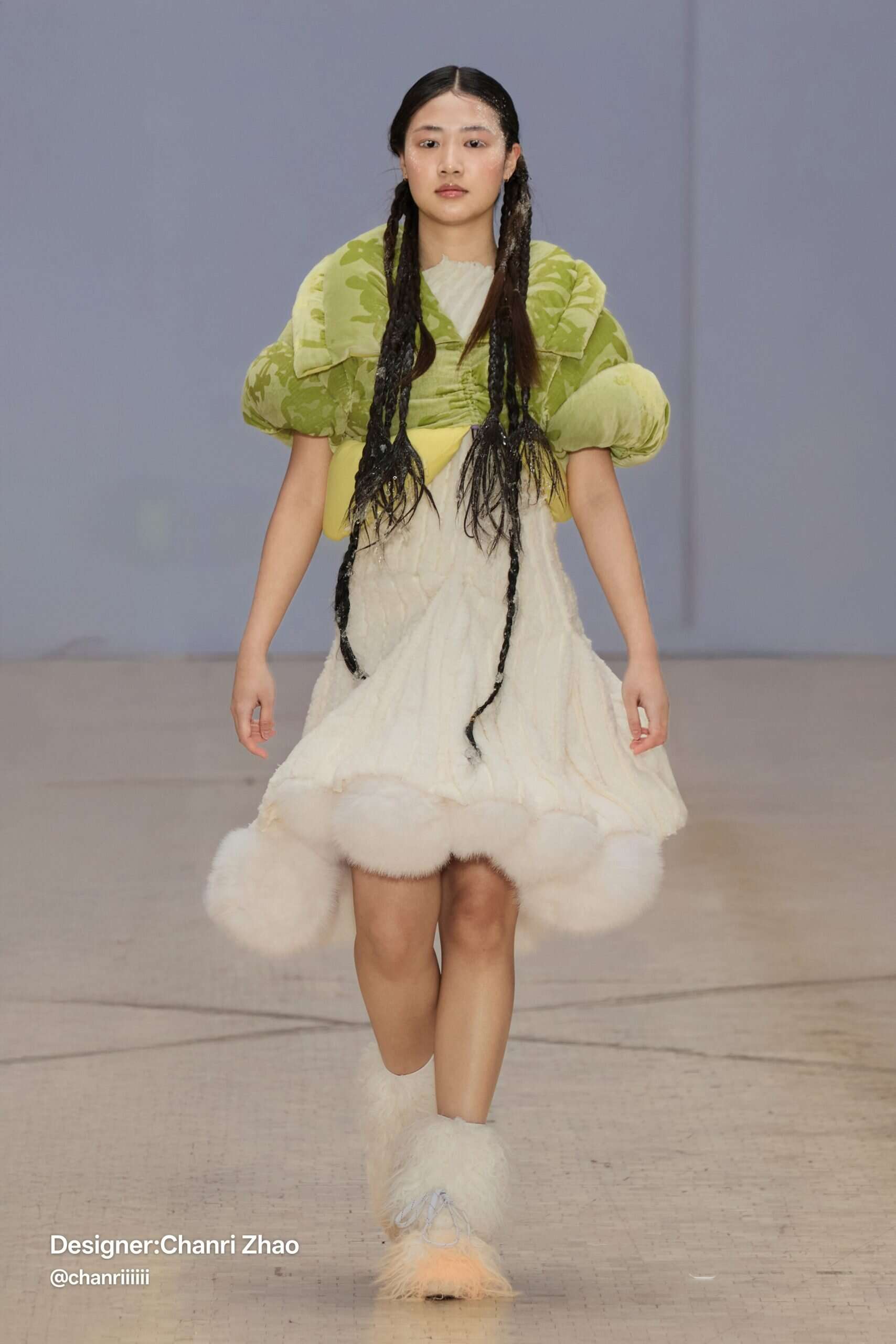 Model wears a cream faux-fur dress with voluminous hem and green sculptural shoulder piece—designed by Chanri Zhao for her graduate collection.
