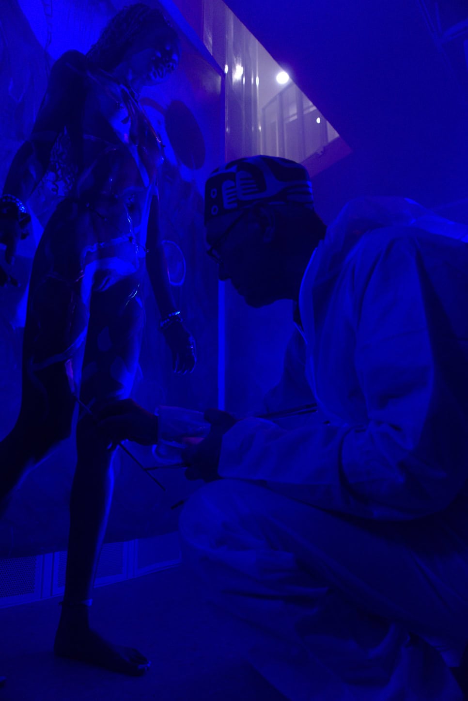 Artist interacting with a sculpture in a blue-lit art installation.