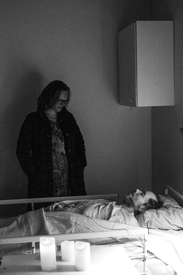 Man standing next to a hospital bed with what appears to be a dead body by Tim Bertram