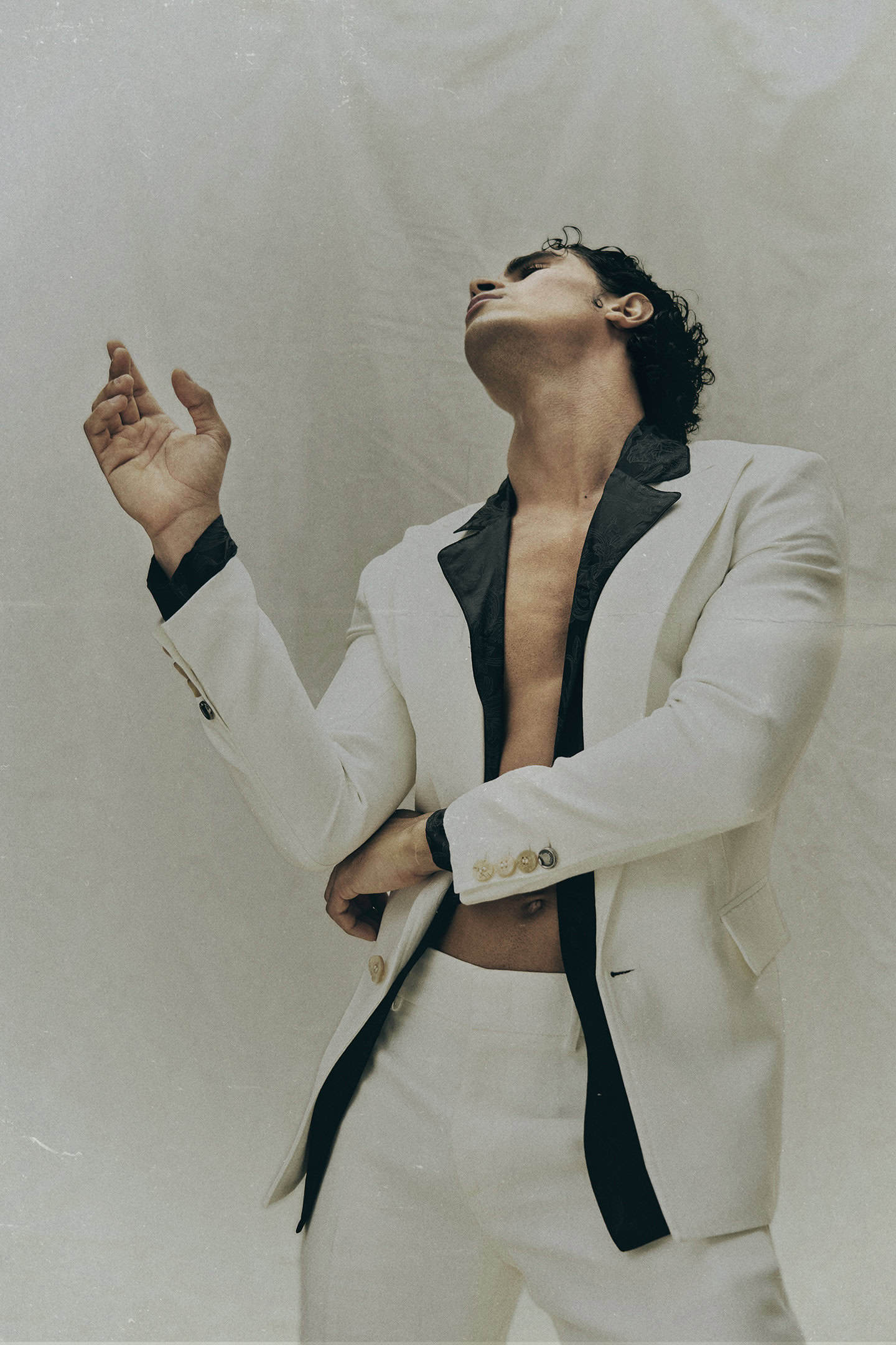 Sad in white tailored suit with black lapels, bare chest, striking pose for Eternal Allure by Ben Cope.