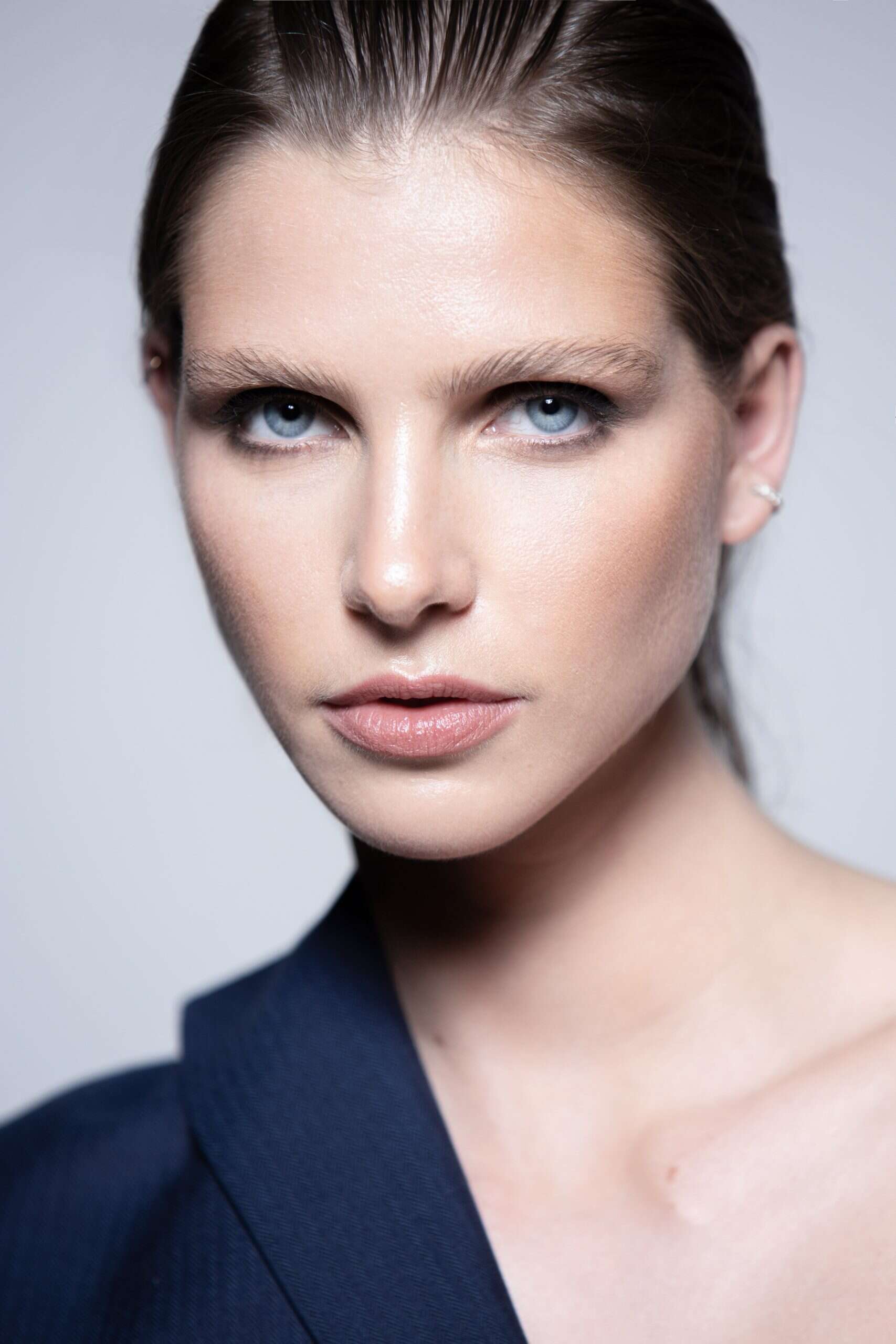 close-up portrait in navy blazer, minimal makeup, sharp gaze, photographed for editorial feature.