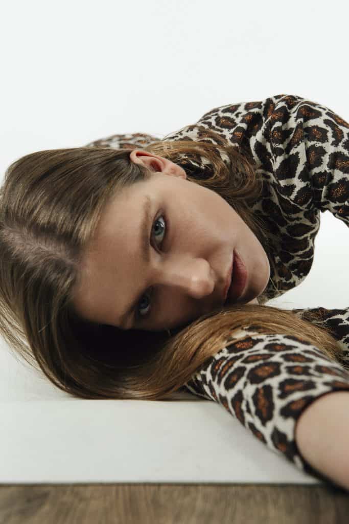 Cornelia in leopard print top, lying down, intense gaze into the lens.