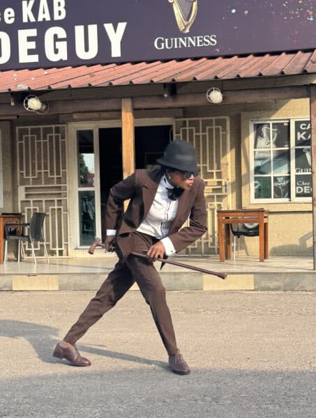 Elegant sapeur dressed in a brown suit, white shirt, and black hat, showcasing Congo's vibrant style.