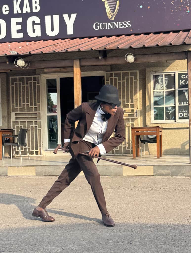 Elegant sapeur dressed in a brown suit, white shirt, and black hat, showcasing Congo's vibrant style.