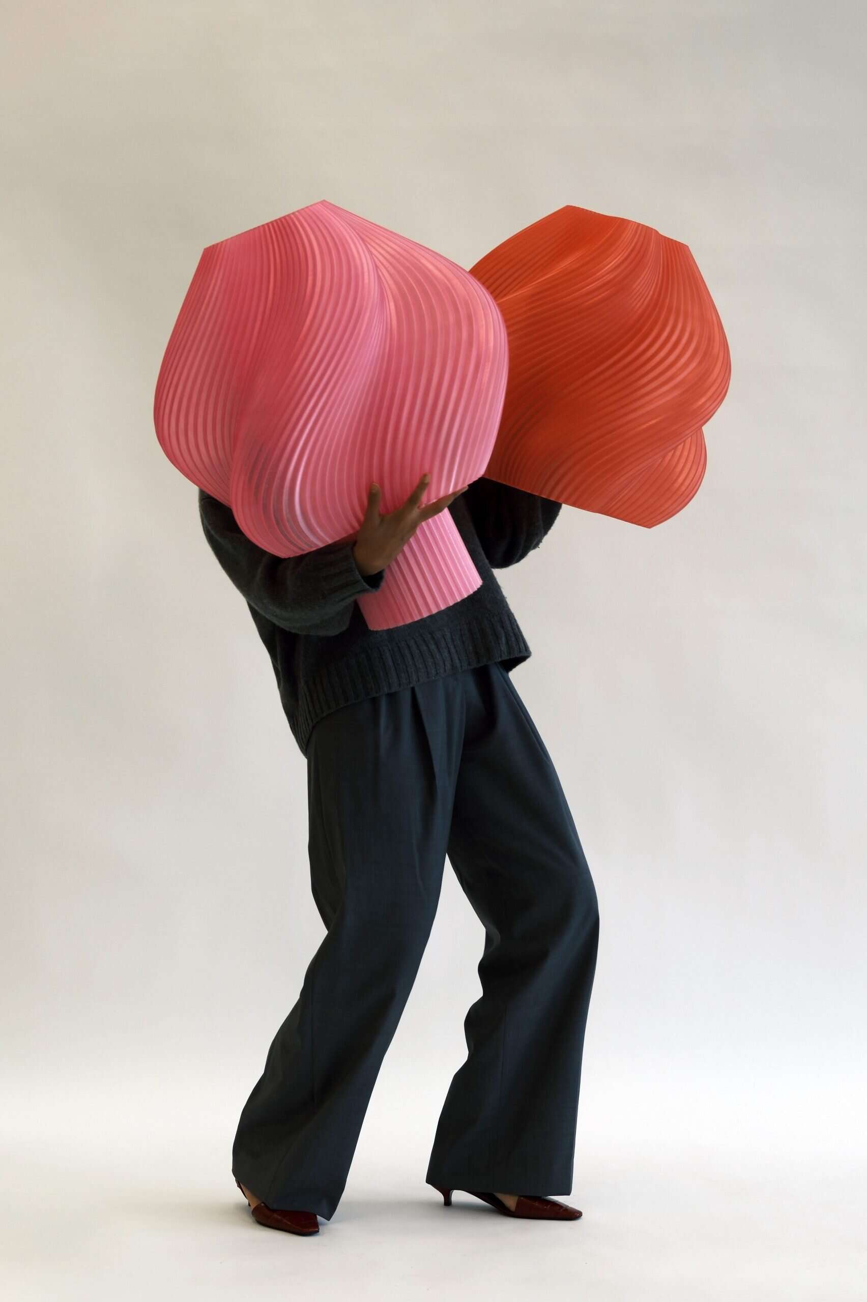 megaheavy Person holding two large, sculptural textile forms—one pink, one red—against a neutral studio backdrop.
