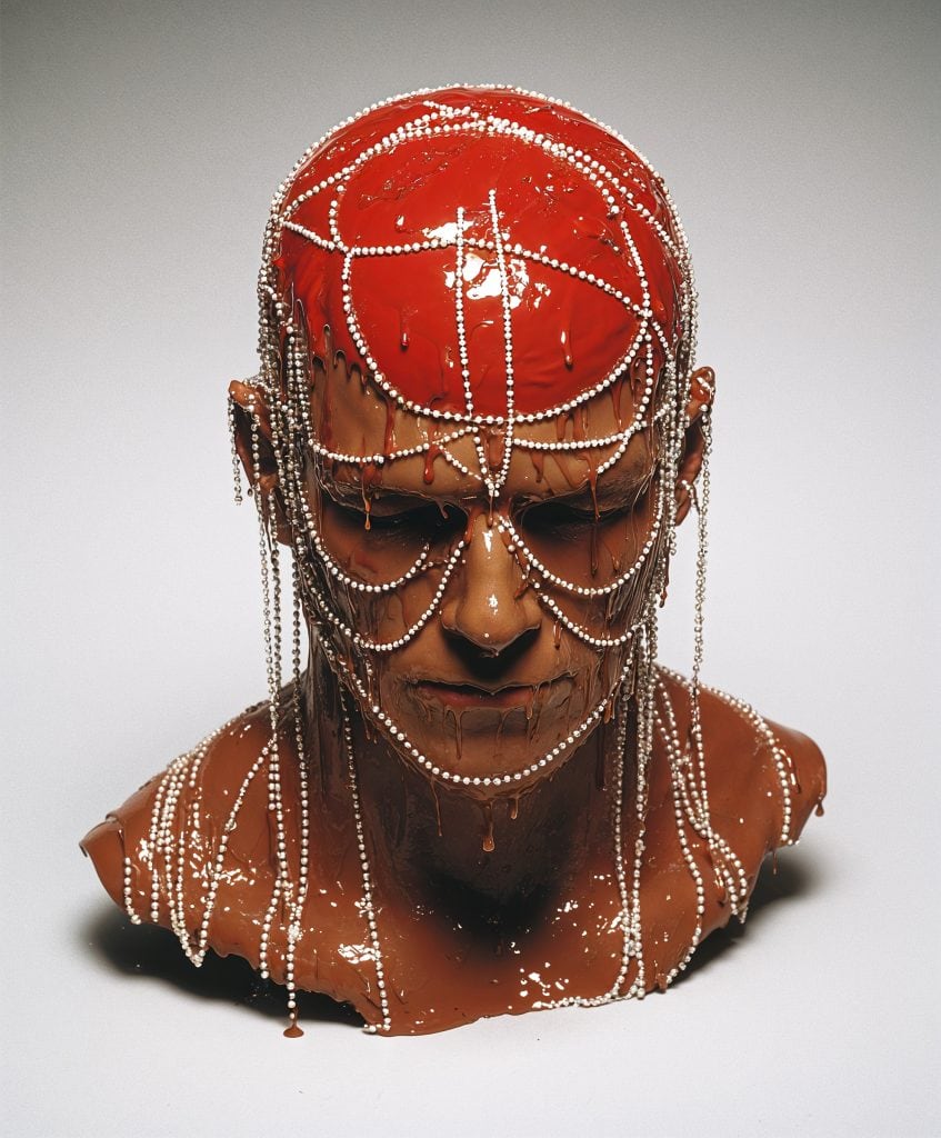 Red-glazed mannequin with white dripping beads and a futuristic face shield, created by Goo Vision