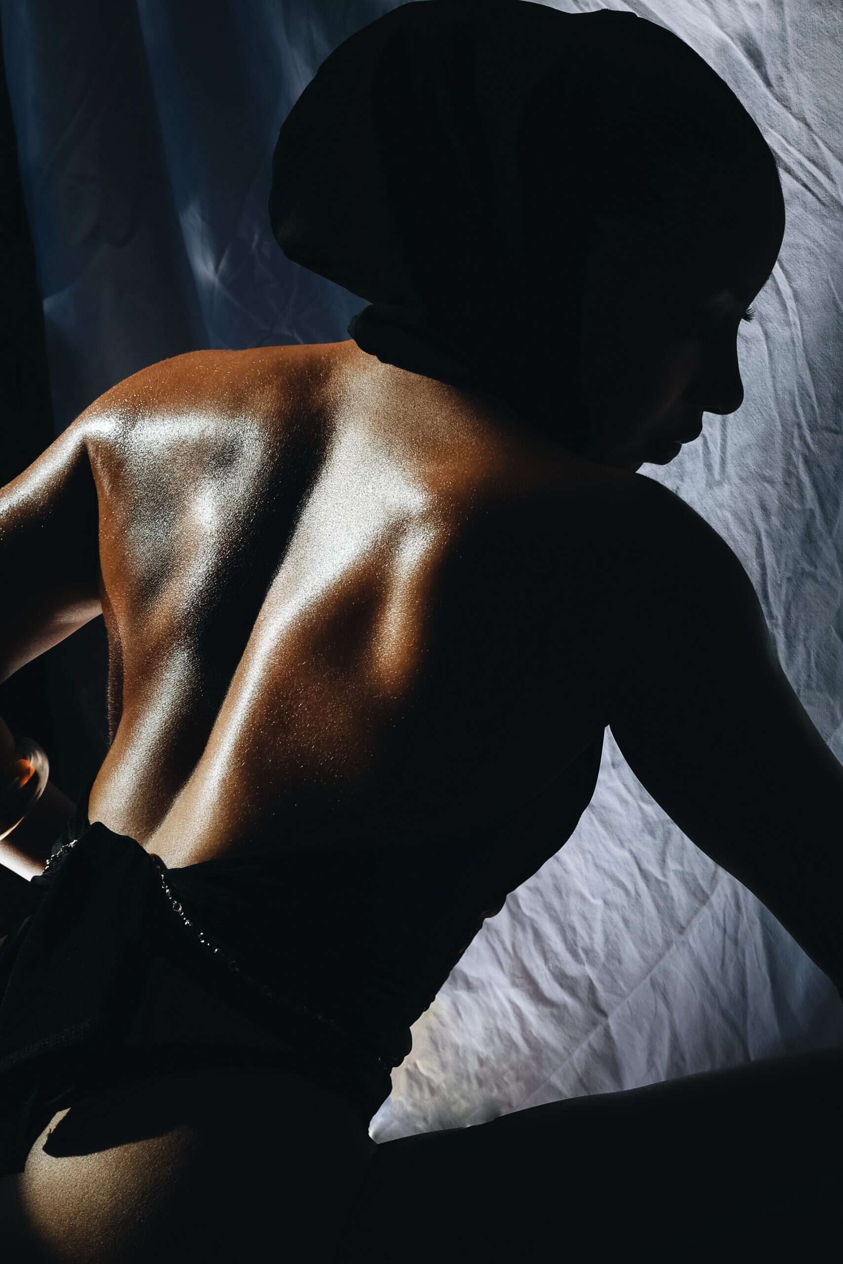 Model Estelle Gisèle poses in silhouette with her back illuminated, skin glistening under dramatic light—photographed by Laurie, makeup by Jade. For undressed to impress 
